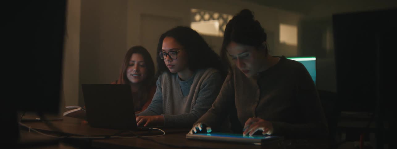 Three women sitting at a table with laptop and tablet working
