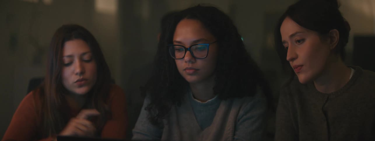 Three young women sitting side by side in front of a laptop