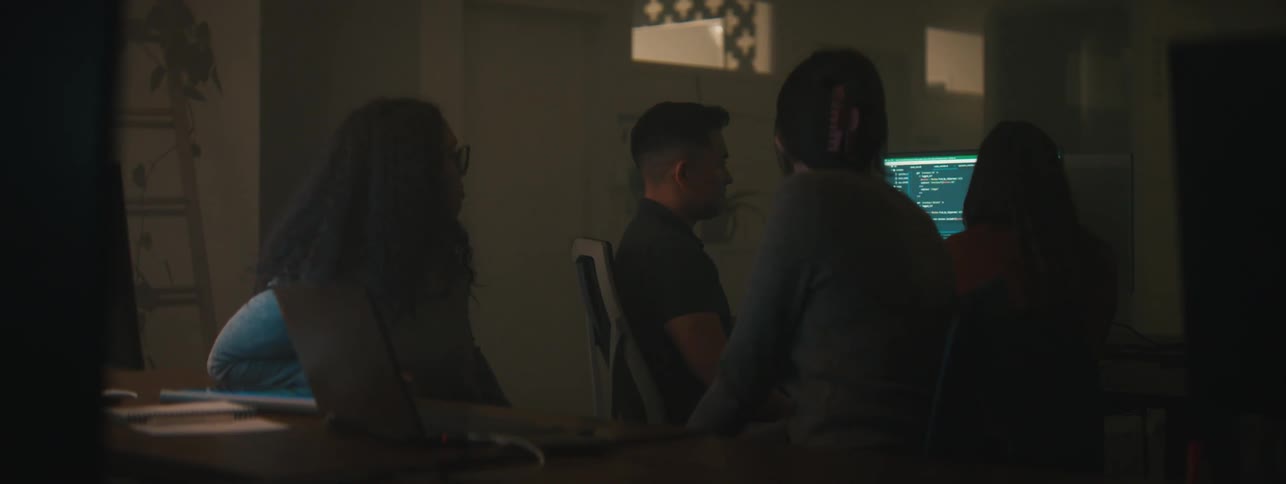 Four people in an office in front of a computer working and talking to each other