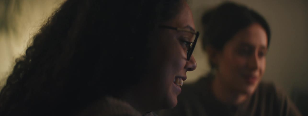 Two women smile and laugh while talking in a room
