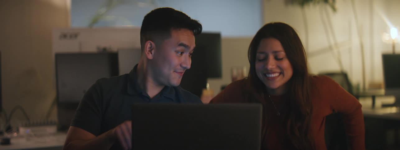 Man and woman sitting in a room talking in front of a laptop