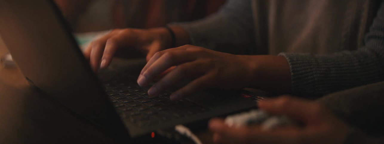 A person typing fast with both hands on a laptop next to another person with a prosthetic right hand