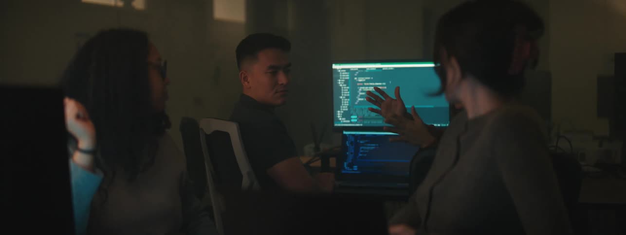 Four people talk while sitting in a computer lab at a school