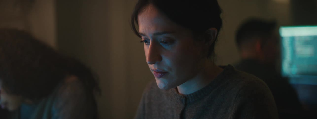 A female student sitting a room with other students reads off of a screen while thinking