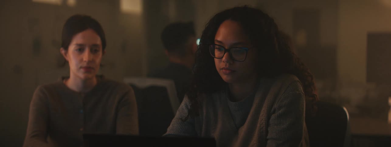 Four people sitting in a dimly lit room in front of a laptop