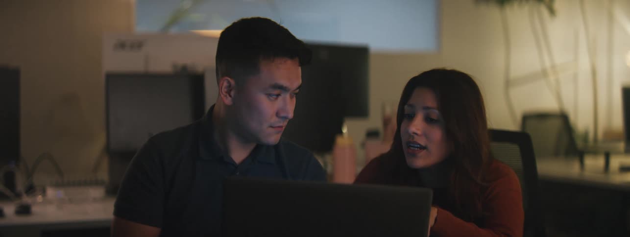 A man and a woman sitting side by side in front of a laptop discussing something in it