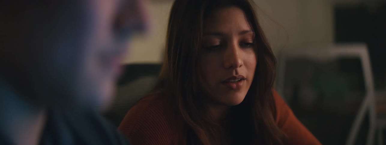 A woman and a man talking while looking at a computer the light from which shines on his face