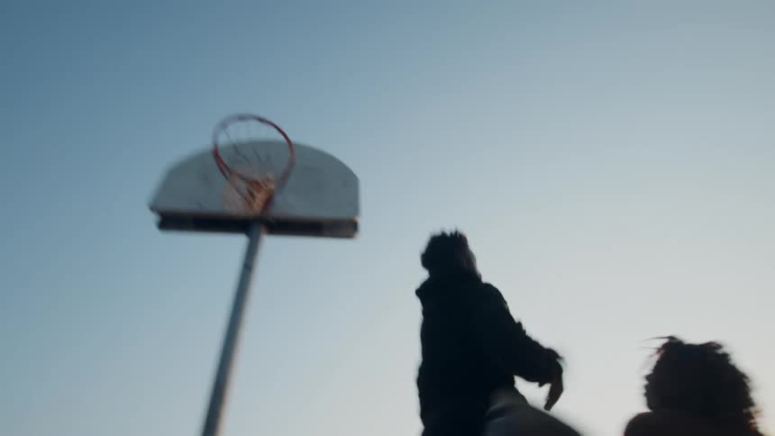 Two black men are playing basketball on an outdoor court at sunset