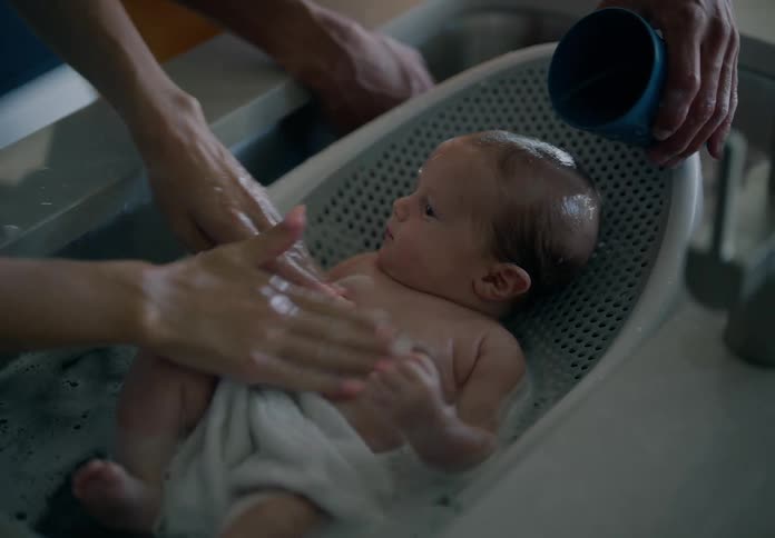 A couple bathing a baby in a sink with soap and a water cup
