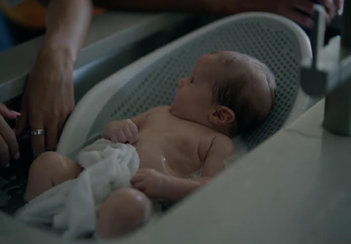 Newborn baby lying in a small bathtub taking a bath