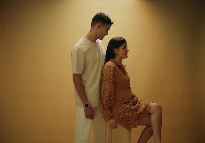Man standing kissing his pregnant wifes forehead as they stand in a studio