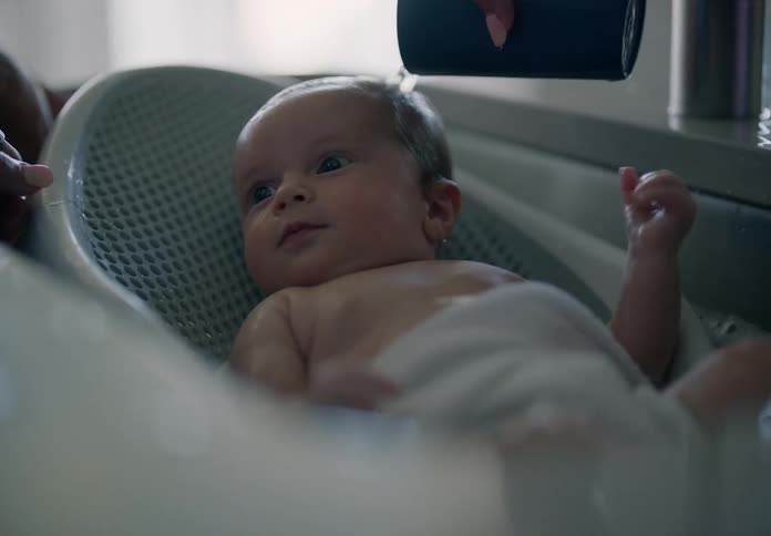 Baby taking a bath lying in a small tub in the sink