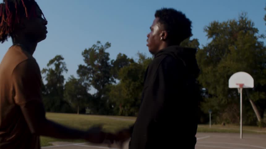 One man pushes another to the ground while they play basketball on an outdoor court