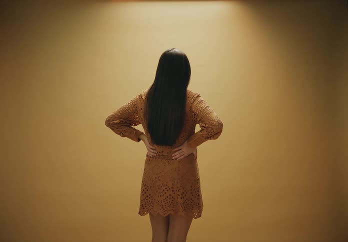 Black haired woman from behind wearing a burnt yellow dress in an indoor room