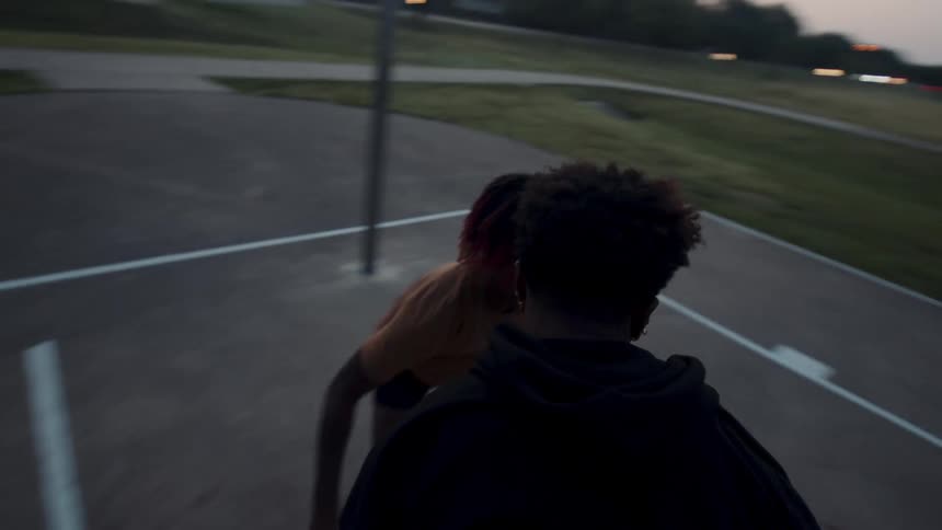 Two boys on an outdoor court playing basketball in the late afternoon