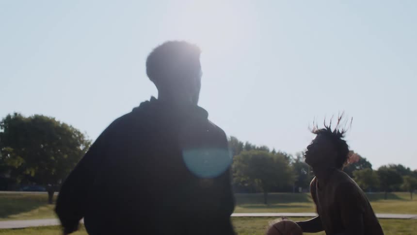 Two young teenagers playing basketball on an outdoor court with trees surrounding