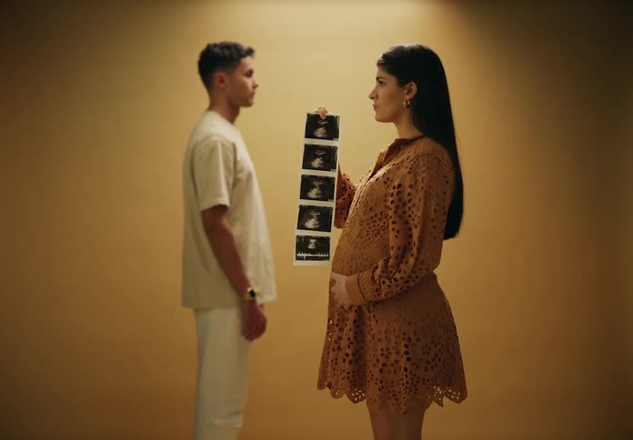 Man in the background and a pregnant woman in the foreground holding ultrasound images