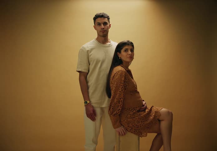 Couple with a man standing next to his pregnant woman posing in a studio
