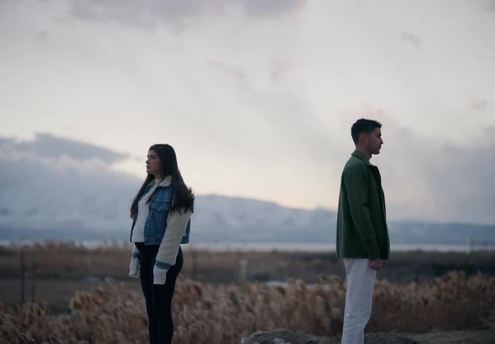 Man with his back to a pregnant woman in a field with the silhouette of mountains on the horizon
