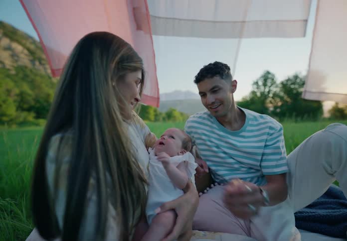 A joyful moment of a couple interacting with their baby under a colorful fabric in a lush green landscape