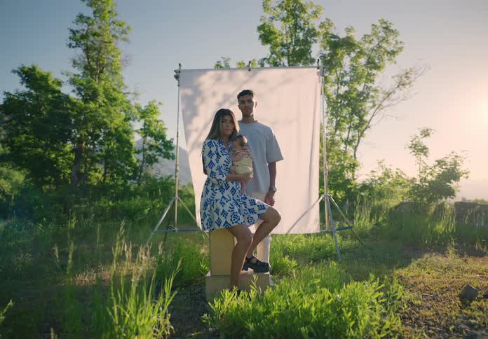 Mother and father pose with their baby in a field against a photography backdrop