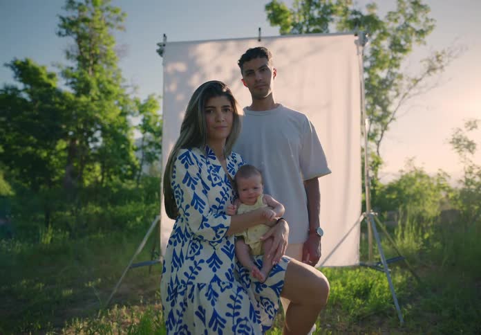 A couple in a clearing in the woods posing with their baby for a photo in front of a sheet working as a screen