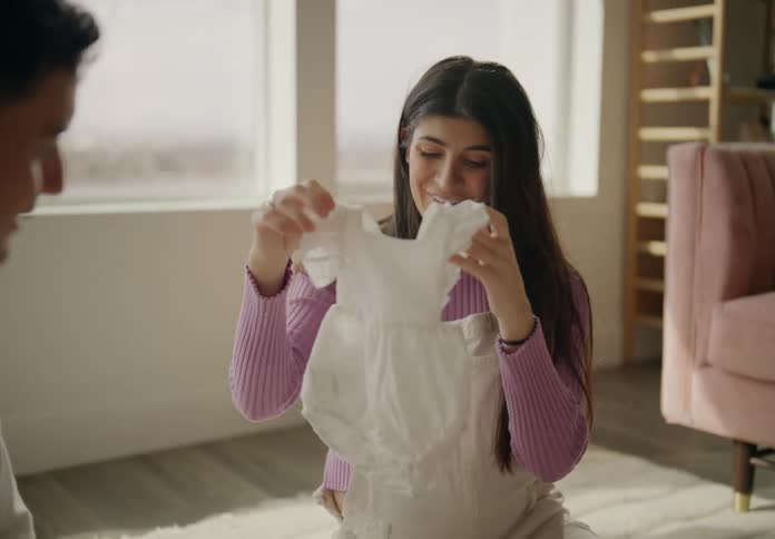 Sitting in the living room with the father an expectant mother smiles while examining baby items that were in a plastic tub