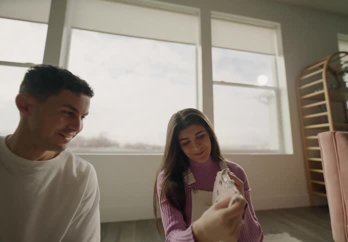 A couple talking and smiling while sitting on the floor picking babys clothes out of a suitcase