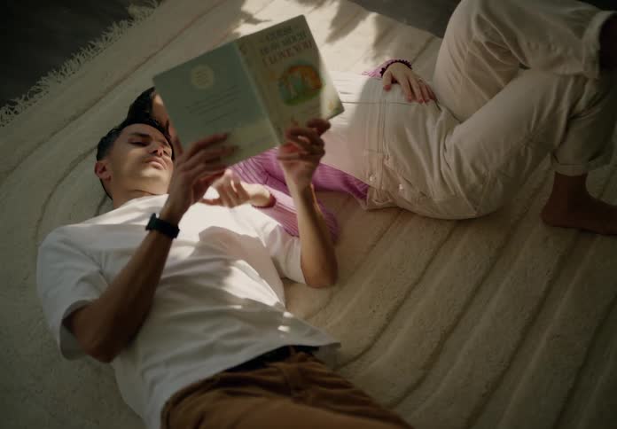 Man and woman lying on the living room rug reading a childrens book