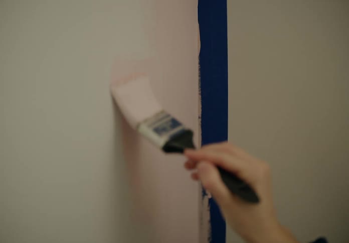 A human hand using a small paintbrush to gently paint a wall pink