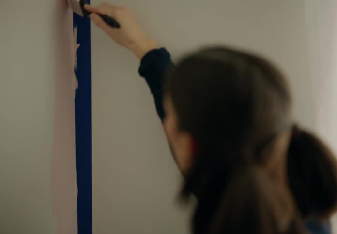 Woman uses a paintbrush to paint a wall pink