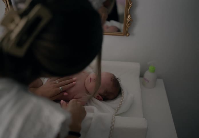 Mother applying cream to her babys body as he lies next to a mirror