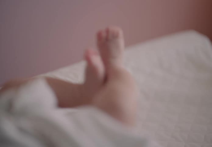 A baby on a blanket moving its legs when a parents hands rub them