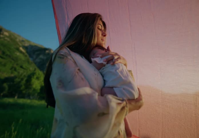 Mother holding her newborn baby in her arms while standing in a grassy backyard with mountains surrounding her