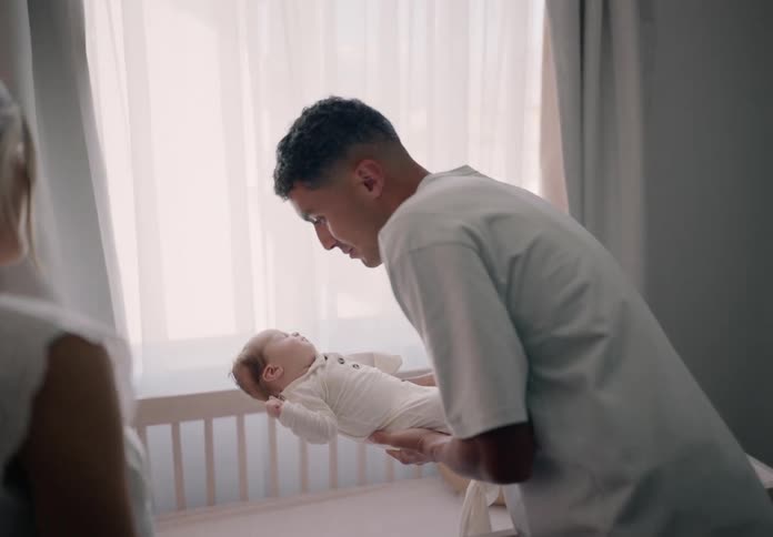 Parents both kiss their baby before laying the child in a crib in the nursery
