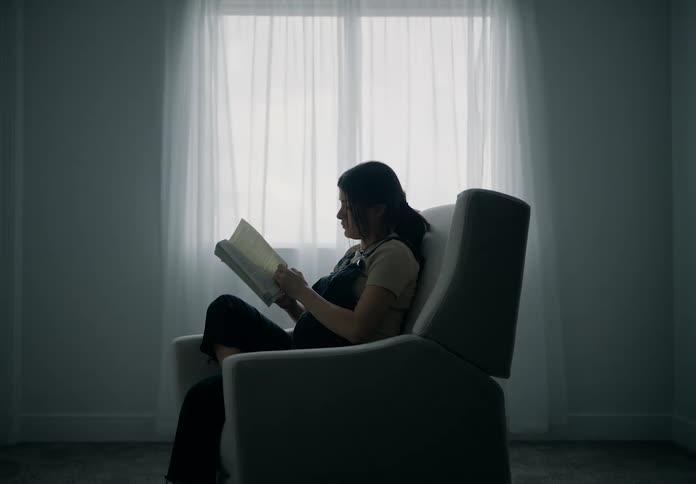 Pregnant woman sits and reads in a recliner