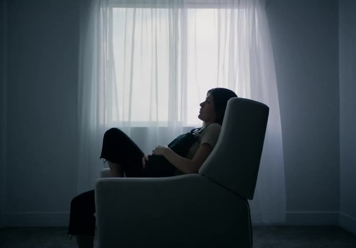 Woman sits in a rocking chair and asks for something from another person in the room