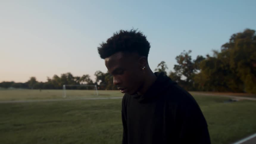 Young man bouncing basketball on the ground on a court with trees in the background