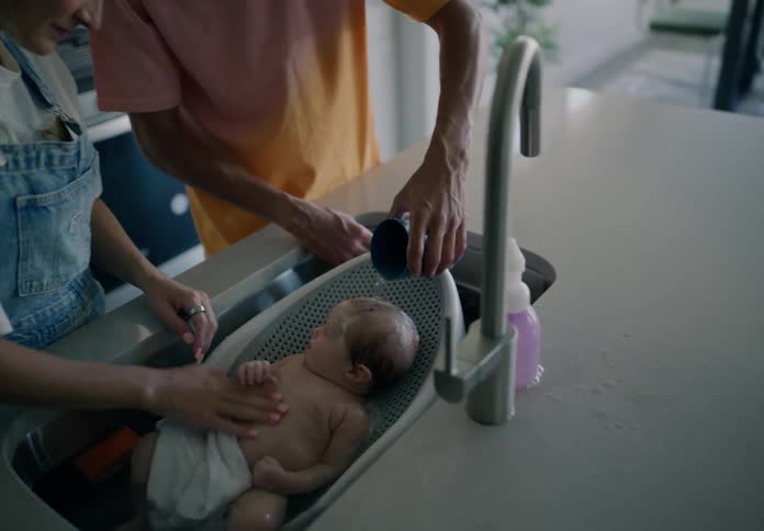 Parents bath their baby in the sink