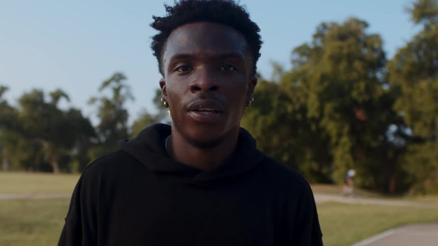 A young man in a black hoodie standing in a park with trees in the background