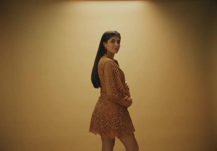 A pregnant woman standing against a beige background wearing a dress