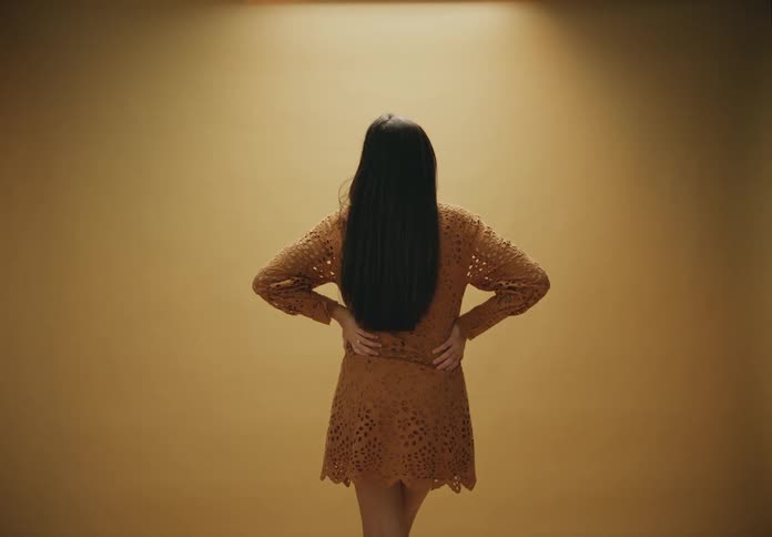 A woman wearing a dress her back to the camera against a beige background