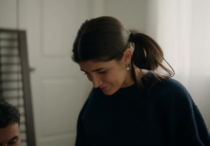 A young woman with her hair tied up was looking down where there is a man pointing forward