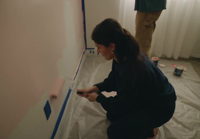 A woman is crouching down and using a paintbrush to paint a wall pink