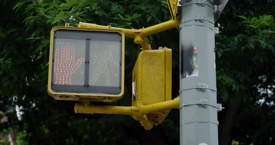 A yellow pedestrian traffic light with a screen hanging next to a pole