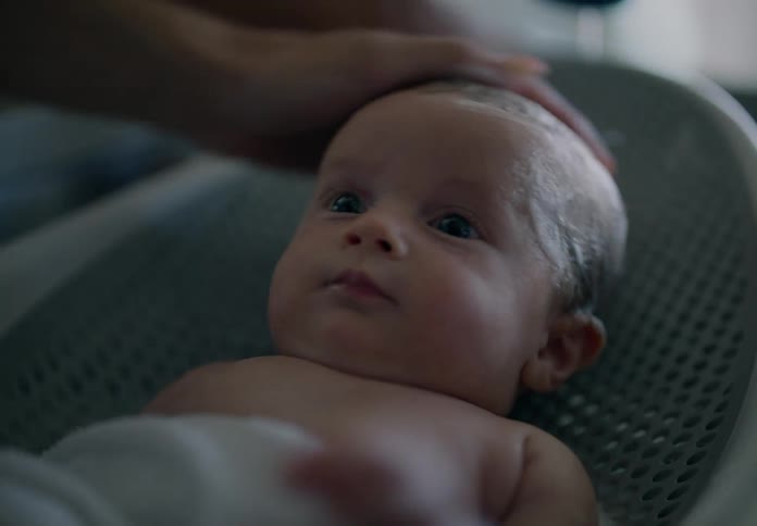 Portrait of a baby lying down with an adults hands giving him a bath