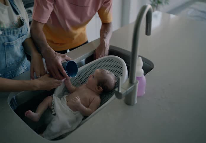 Father and mother bathing a baby in the kitchen sink during the day