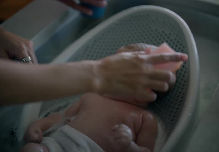 Father and mother together bathing newborn baby in a sink