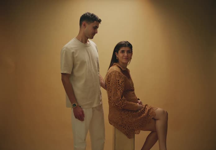 A man standing and a woman sitting and they are talking and smiling on an orange background