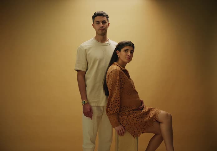 Man standing posing next to his pregnant wife sitting in a chair